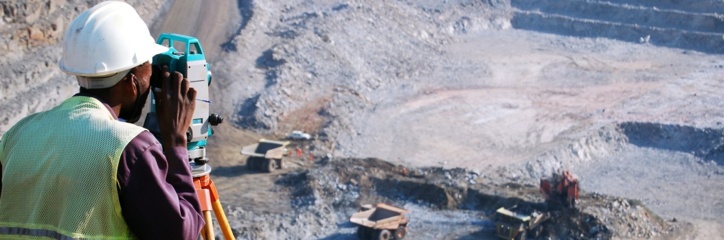 Maarakennustyöntekijä katsoo maanmittauskameran läpi kohti alhaalla olevaa työmaata.