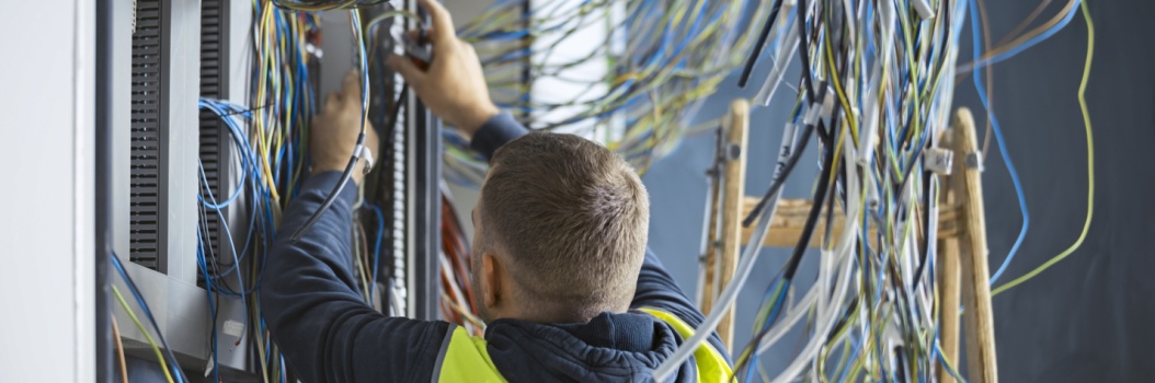 Henkilö seisoo selin kameraan ja säätää sähköjohtoja.