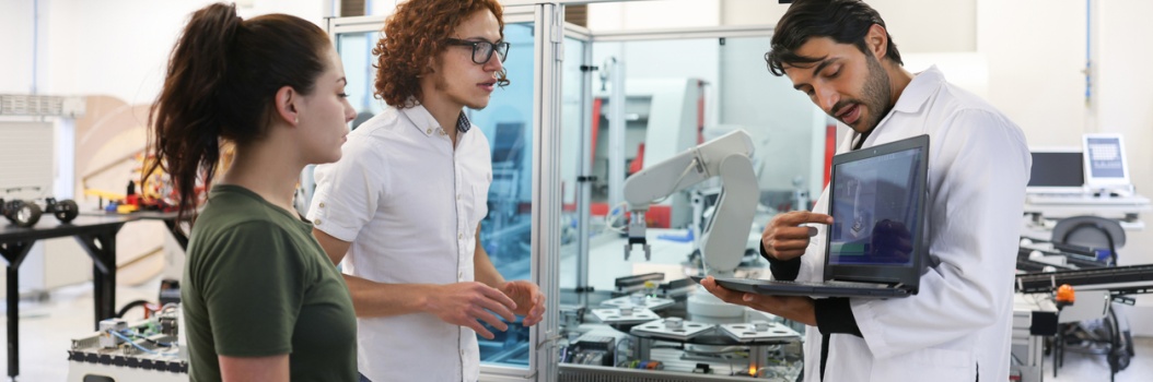 Kolme henkilöä seisoo robotin vieressä. Yksi heistä näyttää muille tietokoneen näytöltä 3D-kuvaa robotista.