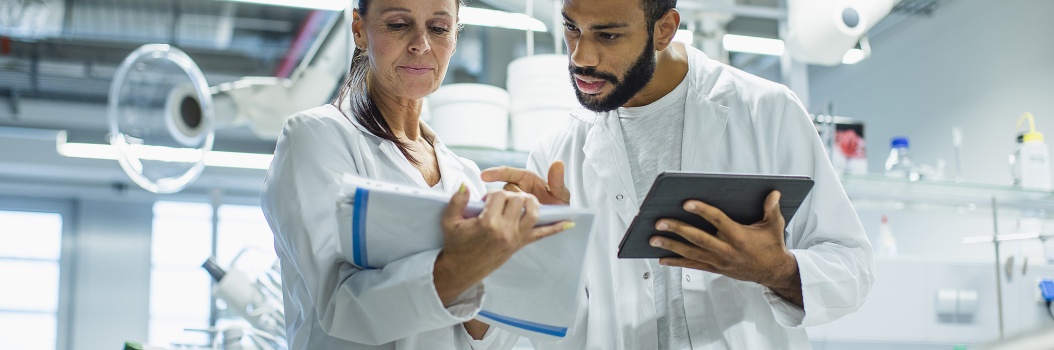 Kaksi valkotakkista henkilöä seisoo vierekkäin laboratoriossa ja katsoo lehtiötä.