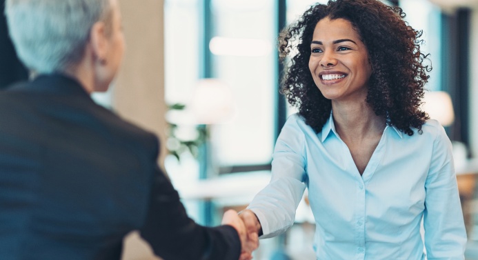 Kaksi hymyilevää henkilöä kättelevät toimistossa.