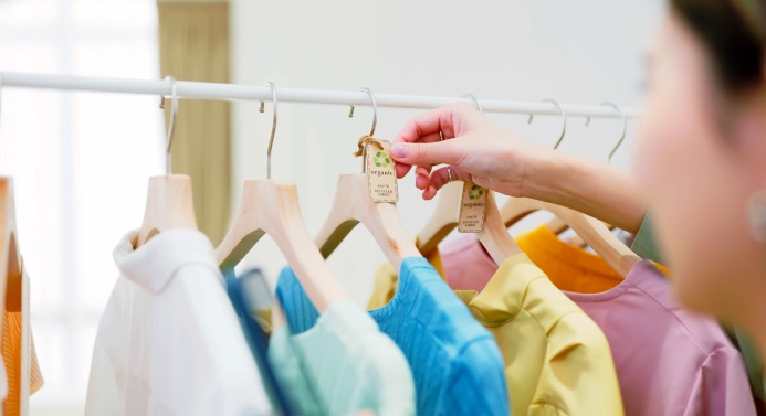 Tummahiuksinen henkilö järjestelee vaaterekkiä, jossa on värikkäitä vaatteita.