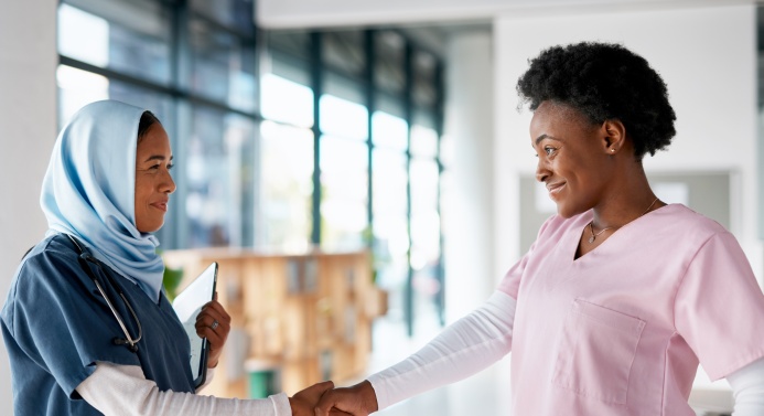 Kaksi hoiva-avustajaa kättelee ja katsoo toisiaan silmiin hymyillen.