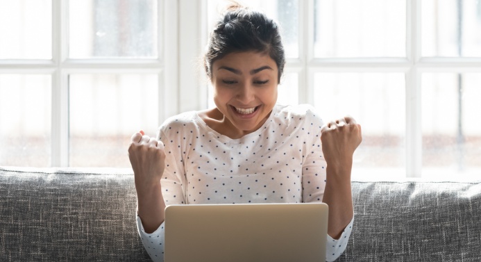 Innostunut henkilö istuu sohvalla kannettava tietokone sylissä.