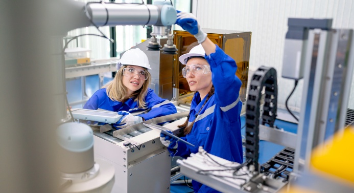 Kaksi työntekijää käyttää robottia teollisuushallissa.