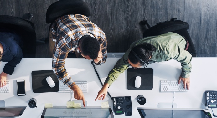 Lintuperspektiivistä kuvattu kaksi henkilöä tietokoneiden ääressä osoittamassa samaa näyttöä.