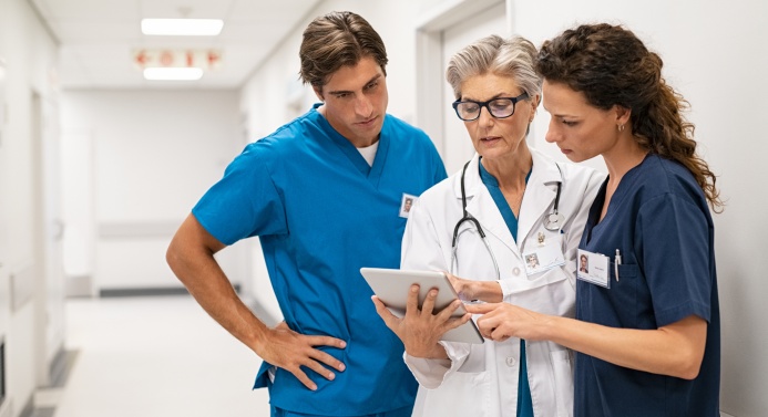 Kaksi hoitajaa ja lääkäri keskustelevat ja katsovat paperia yhdessä sairaalan käytävällä.