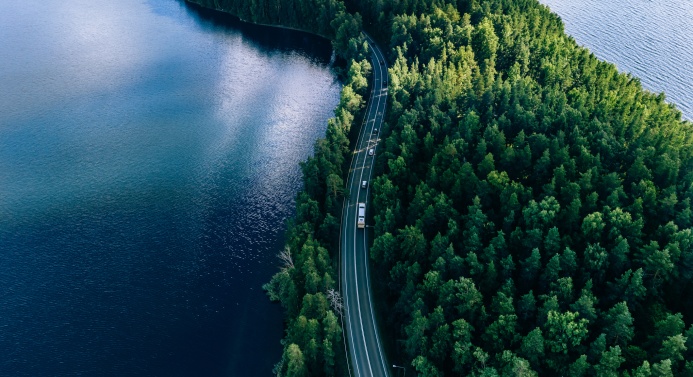 Lintuperspektiivistä metsätie järvimaiseman keskellä.