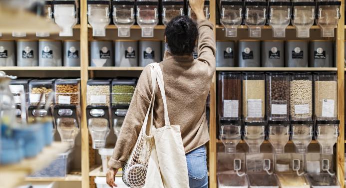 Nainen kurottaa kaupassa tuotetta ylähyllyltä.