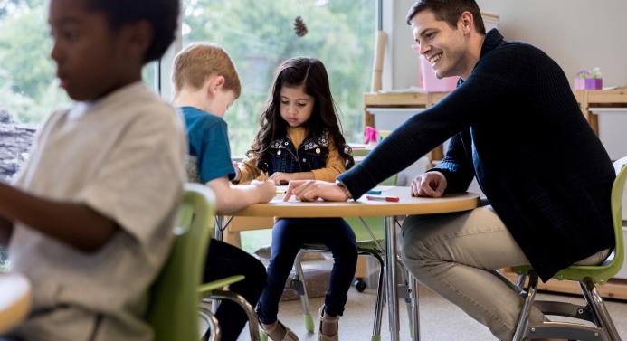 Varhaiskasvatuksen opettaja istuu lasten kanssa pöydän äärellä ja ohjaa lapsia.